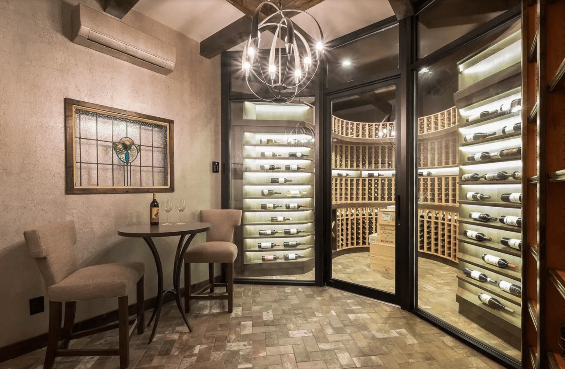 Luxury custom wine cellar with glass doors, curved wood racking, and tasting area seating