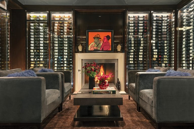 Luxury wine cellar lounge with glass-enclosed racking, wood millwork, fireplace seating, and integrated display lighting.