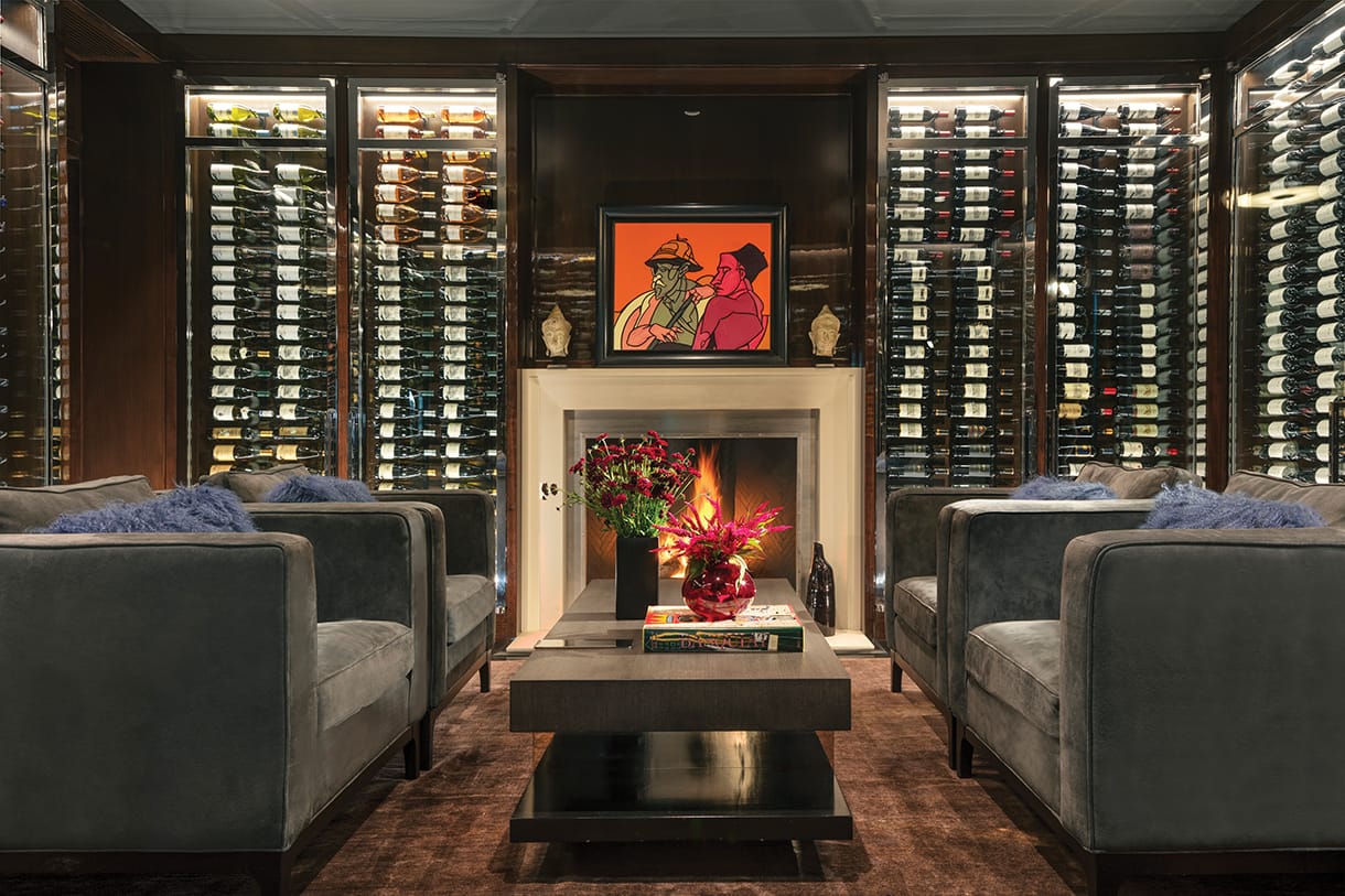 Luxury wine cellar lounge with glass-enclosed racking, wood millwork, fireplace seating, and integrated display lighting.