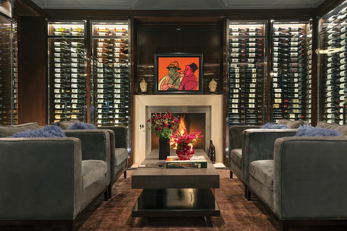 Luxury wine cellar lounge with glass-enclosed racking, wood millwork, fireplace seating, and integrated display lighting.