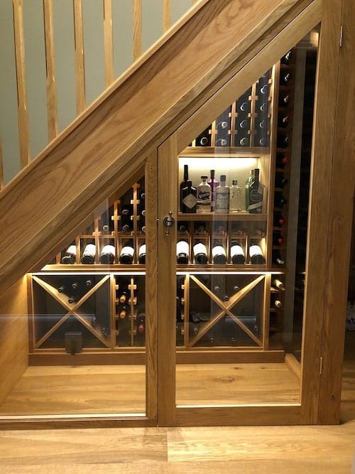 Residential under-stair wine cellar with custom wood cabinetry, glass door, and integrated bottle storage racks